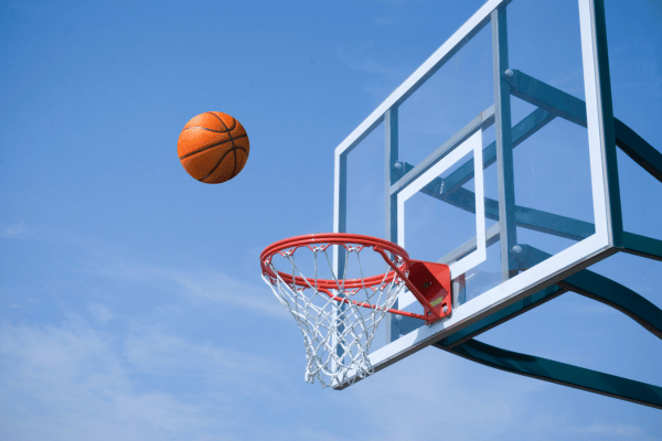 A basketball is mid-air near a hoop under a clear blue sky on an outdoor court.