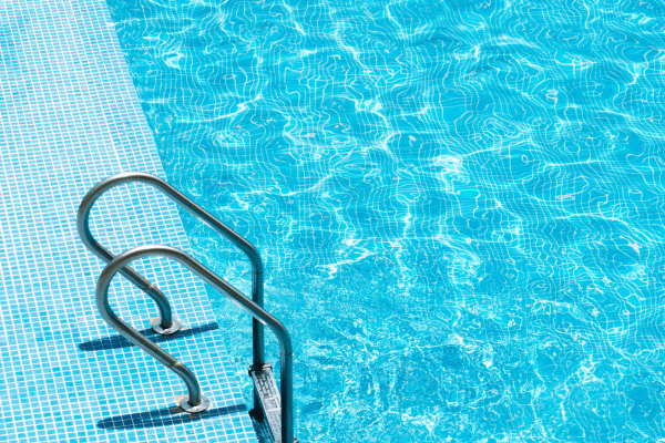 A clear blue swimming pool with a metal ladder and tiled edge, reflecting sunlight on the water